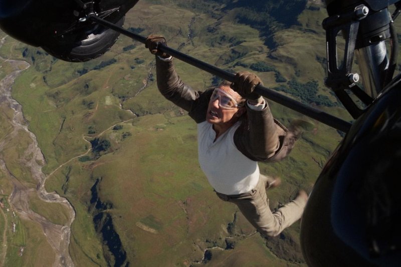 Tom Cruise as Ethan Hunt hanging from beneath the bar of a high-flying biplane.